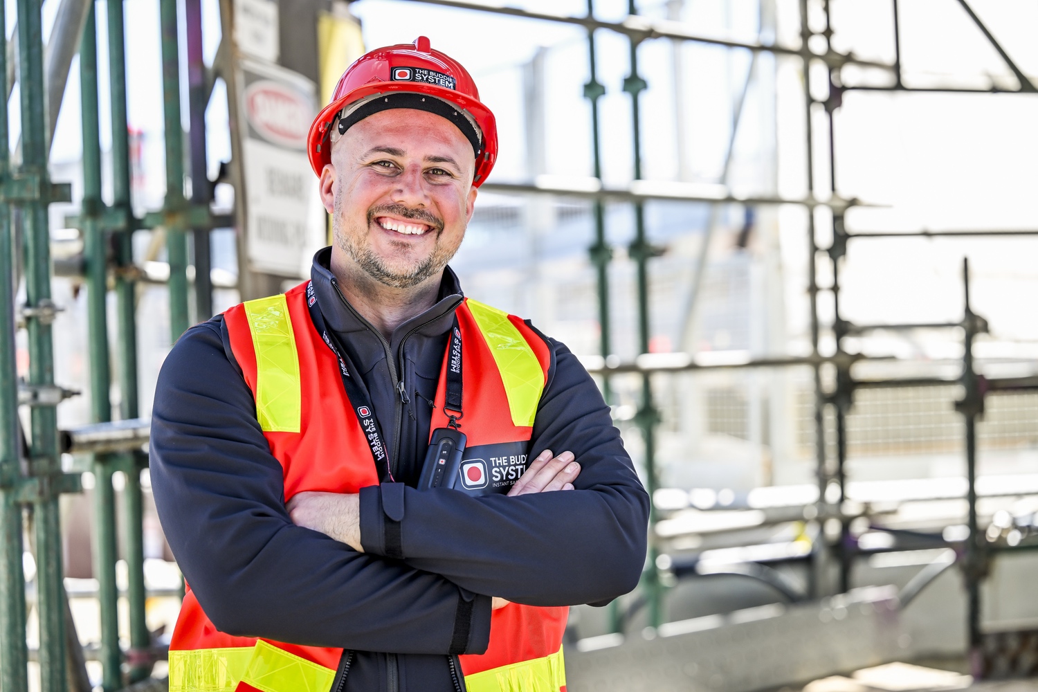 Crew member on scaffolding wearing The Buddie System branded vest and hard hat