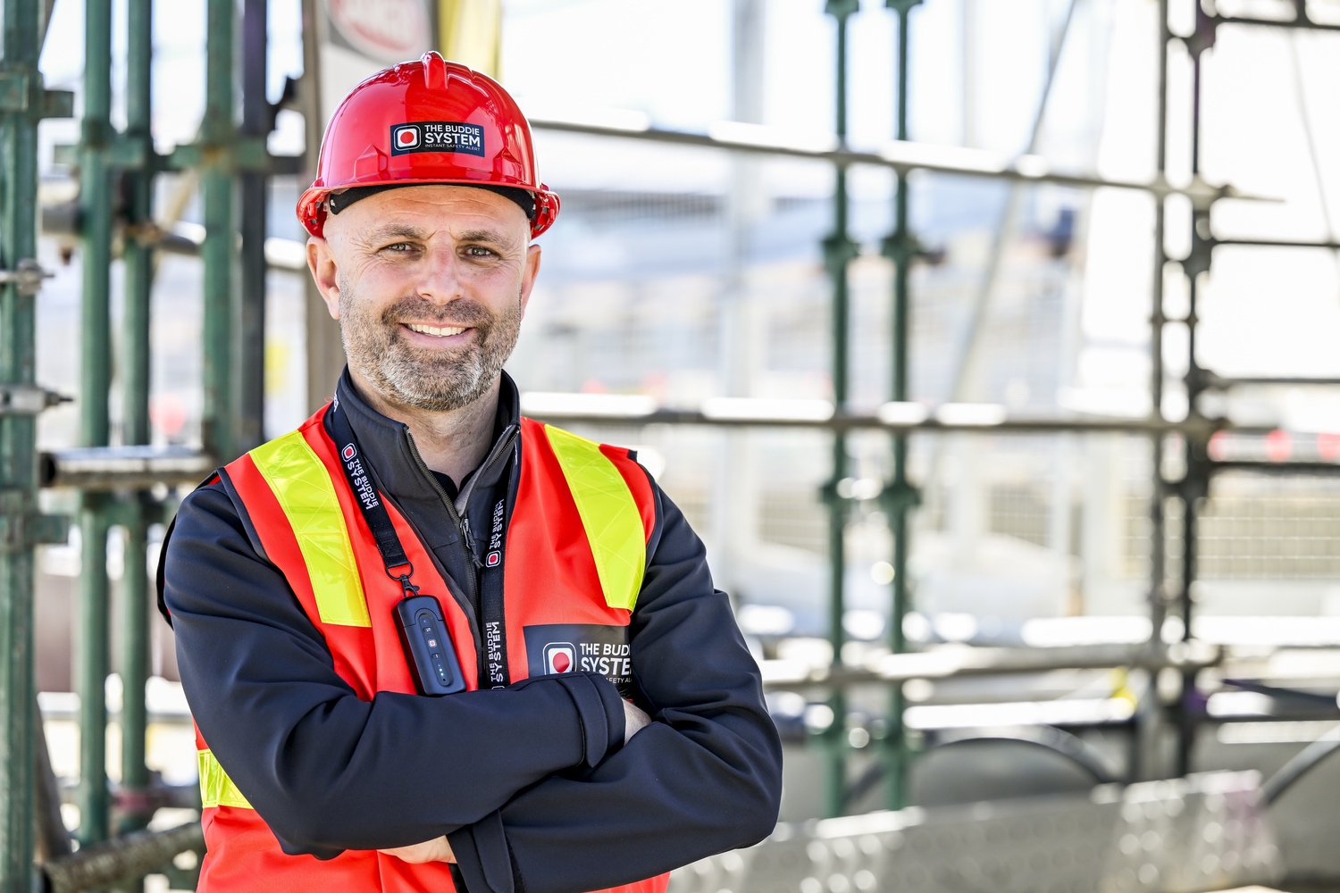 Smiling foreman in a red Buddie System hard hat and hi-vis vest on a steel jobsite